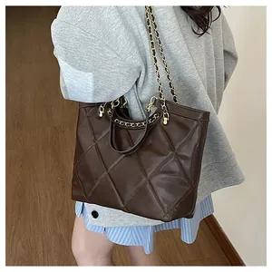 Side view of a dark brown quilted chain tote bag with gold straps carried by a model