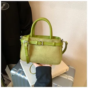 Vintage green matte crossbody handbag held over a book and silver travel suitcase.