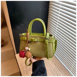 Close-up of green frosted retro handbag with cute pom-pom charms and buckled straps.
