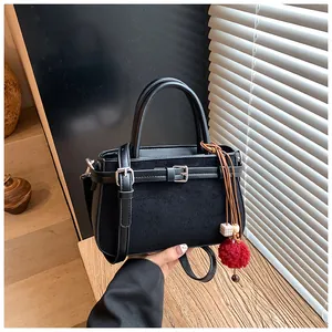 Detail view of a black matte vintage handbag with red pom-pom charm and buckle strap.