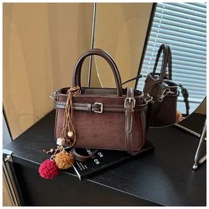 Detailed shot of a vintage brown suede bucket bag featuring decorative pom-poms on a desk