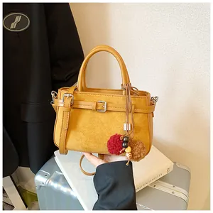 Detail view of a vintage ginger yellow frosted crossbody handbag with pom-poms