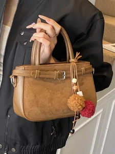 Vintage brown suede handbag with decorative buckle strap and plush pom-pom charm