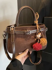 Vintage brown suede handbag with decorative pom-pom charms for autumn and winter.
