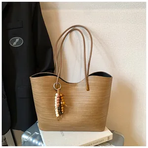 Detailed view of large brown woven tote bag with bead charm in a lifestyle setting