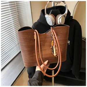 Close-up of large brown textured tote bag with decorative bead charm and shoulder straps.