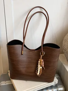 Stylish large brown woven leather tote bag featuring long straps and a beaded charm