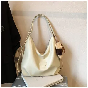 Vista dettagliata della borsa tote versatile crema con ciondolo a orsetto su una valigia.