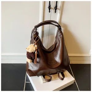 Dettaglio di una grande borsa marrone vintage con ciondolo a orsetto su base bianca