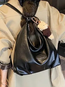 Borsa tote vintage nera capiente indossata come zaino sopra un trench beige moderno