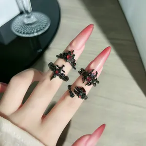 Primer plano de anillos góticos negros con pedrería roja y diseño de araña y cruz