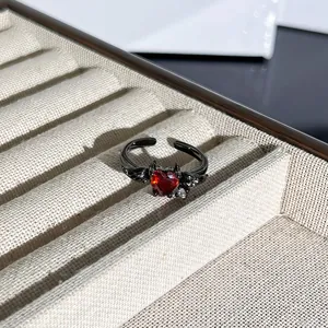 Detalle macro de un anillo gótico negro con una piedra de corazón rojo y alas de murciélago.