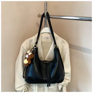 Large black leather tote bag with cute bear charm hanging on a stylish cream coat.