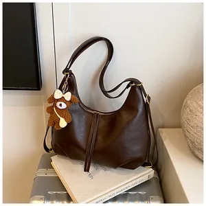 Large brown faux leather hobo shoulder bag with cute teddy bear charm on a vintage suitcase
