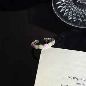 Gedetailleerde close-up van een zilveren emaille open ring met roze en groene details.