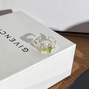 Detailansicht eines silbernen Rings mit grüner Schmetterlingsschleife und Perlen.