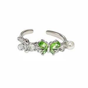 Detailansicht eines silbernen verstellbaren Rings mit grünem Schmetterling und Perlen.