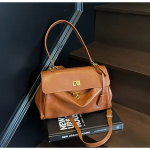 Vintage brown faux leather shoulder bag with metallic lock detail on dark stairs.