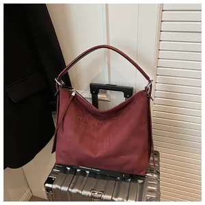 Detalle de un bolso tote de ante burdeos sobre una maleta plateada de viaje