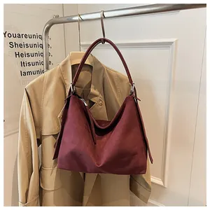 Bolso tote grande de ante granate colgado en un perchero con gabardina de fondo.