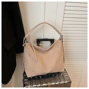 Bolso tote grande de ante beige con asa única sobre una maleta plateada para viaje