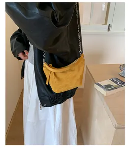 Close-up of a model wearing a trendy yellow suede crossbody dumpling bag with silver chain strap