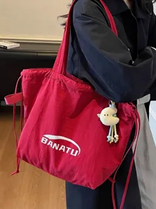 Large red canvas drawstring tote bag with plush charm, casual style shown on model