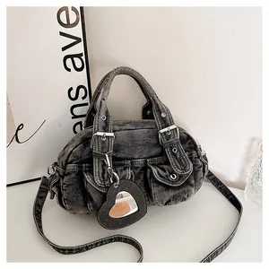 Close-up detail of a dark wash denim boston bag featuring front pockets and a heart mirror charm.