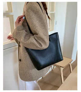 Detailed view of a large black minimalist leather tote bag worn over the shoulder.