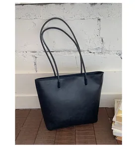 Minimalist black tote bag with long straps displayed against a white brick wall