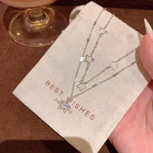 Detailed macro view of a dainty layered silver star necklace on a cream gift pouch