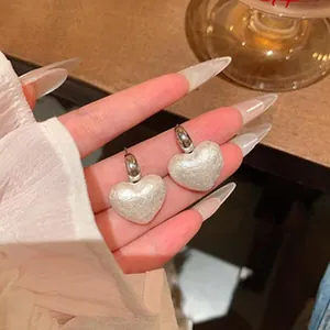 Close-up detail of elegant white pearlescent heart-shaped earrings with silver hooks