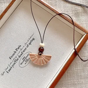 Macro view of a fan-shaped woven pendant necklace on a rustic wooden tray.