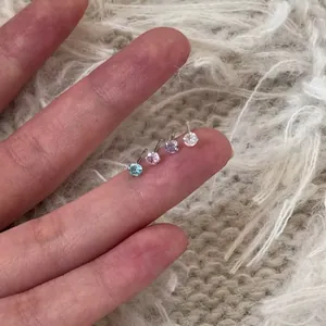 Detailed macro view of four sparkling colorful zircon stud earrings held on a fingertip