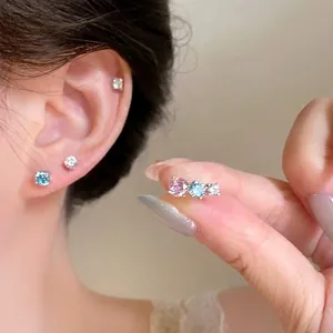 Close-up detail of shiny pink and blue cubic zirconia stud earrings worn on a female ear