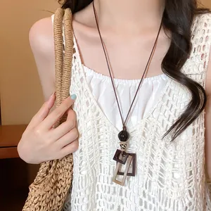 Geometric wood pendant necklace on a braided rope cord styled with a white crochet top