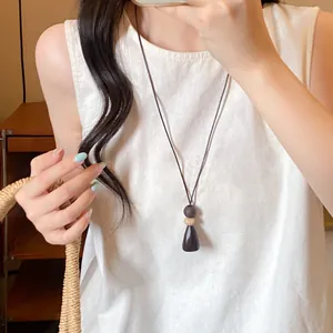 Long wooden geometric pendant necklace on a minimalist cord worn with white top