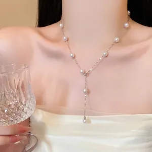 Detail of elegant Y-shaped silver necklace with white pearls worn by model in white dress.
