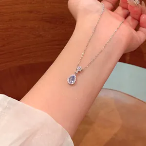 Close-up of silver water-drop necklace with a light blue crystal pendant on arm