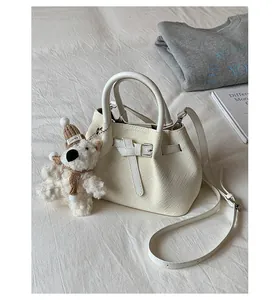 Stylish cream white woven bucket handbag featuring a cute teddy bear charm on cozy bedding
