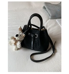 Close-up of black woven bucket bag with a cute white teddy bear charm on white bed.