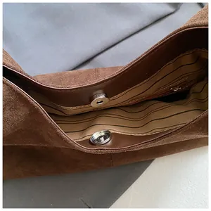 Interior detail of brown suede hobo bag showing striped lining and magnetic snap closure.