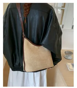 Detail shot of a large beige suede shoulder bag with brown leather trim on a model.