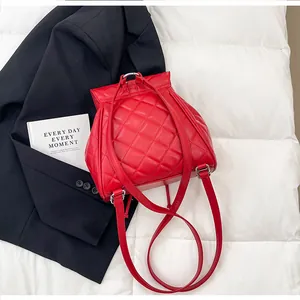 Vue arrière d'un mini sac à dos rouge matelassé avec clips métalliques sur un lit