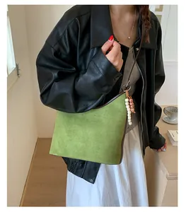 Close-up of a green suede retro bucket bag with a stylish beaded charm accessory.