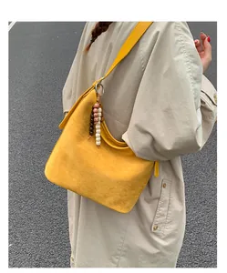 Model wearing a yellow suede shoulder bag with beaded charm in a lifestyle setting.