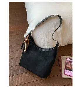 Vintage black suede bucket bag with beaded tassel on a neutral indoor background