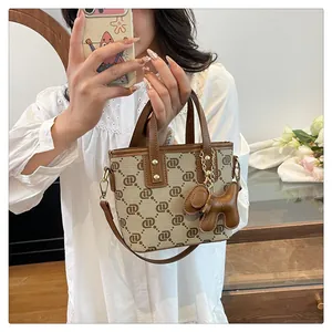 Close-up of a stylish monogram bucket bag with dog charm held by a woman in white shirt