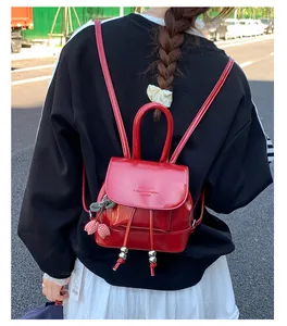 Close-up of a stylish red mini backpack with charms worn by a model in a street setting