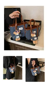 Detail van denim emmertas met bruine lederen afwerking en een schattige teddybeerhanger